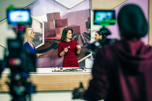 Rear view photo of a cameraman operating two cameras while filming a make-up infomercial for television.