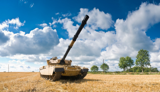 Large military tank guarding rural perimeter.