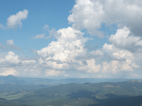Cloudy sky above the mountain range. Carpathians mountains at summer, west Ukraine. White cumulus floating in blue sky. Green forest on hillsides. Ukrainian nature landscape. Blurred background