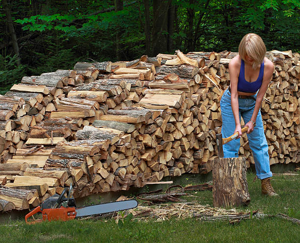 Sexy women lumberjack cutting firewood in front of woodpile