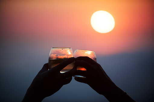 Two female hands holding glasses with drinks celebrating a toast sundowners at sunset high above the clouds Cape Town South Africa