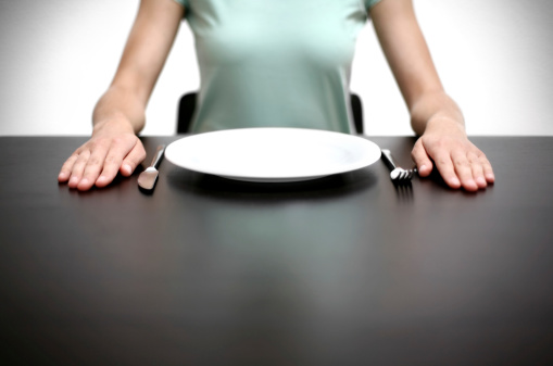 woman sitting on a table. in front of an empty plate, knife and fork. Waiting for lunch.