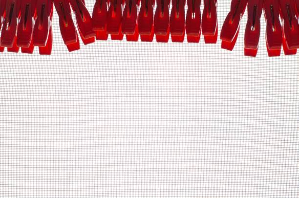 Red color clothespins putting on mosquito wire screen window isolated on white background with space for text.