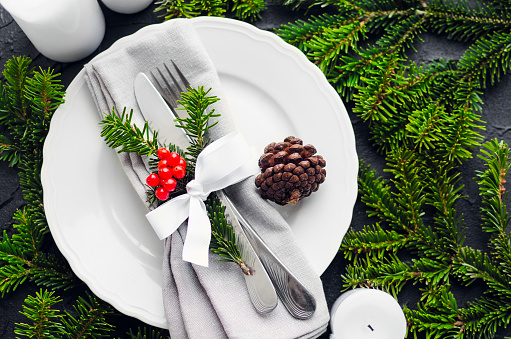 Festive Christmas and New Year table setting in scandinavian style with natural decor. Dining place decorated with green fir tree branche and pine cones. Holiday Decorations. Top view.