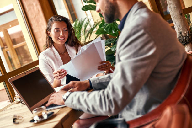 istock Business lunch. Man sitting at table working on laptop at restaurant while woman reading documents smiling cheerful close-up 1051879768