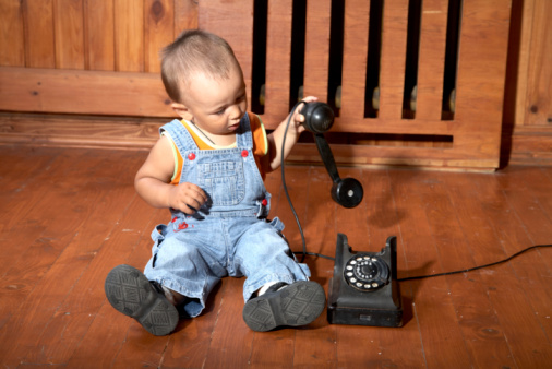 The little boy plays old phone sitting on a floor