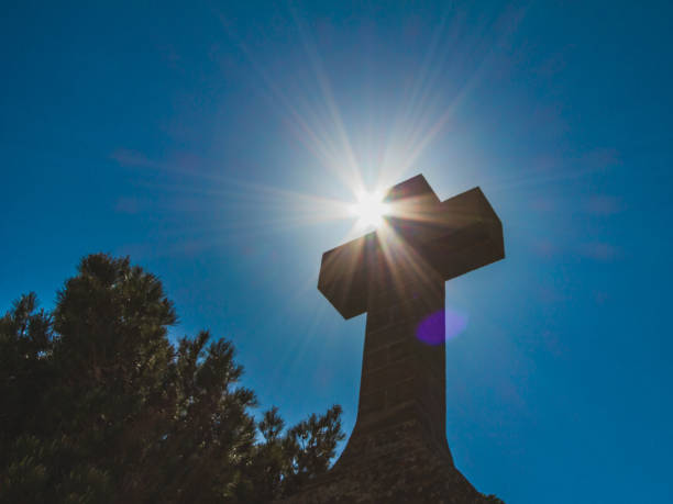 istock Christian stone cross on dark blue sky background against sun. Religious concept 1051910372
