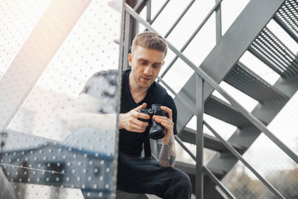 Attractive man sitting at staircase and checking photos in camera.