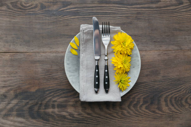 Rustic table setting with linen napkin, cutlery, ceramic plates, yellow glasses and yellow flowers