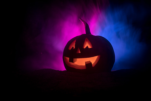 Halloween pumpkin smile and scrary eyes for party night. Close up view of scary Halloween pumpkin with eyes glowing inside at black background. Selective focus