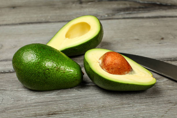 istock Two avocados, one cut in half, seed visible, knife next to it, on gray wood desk. 1052017402