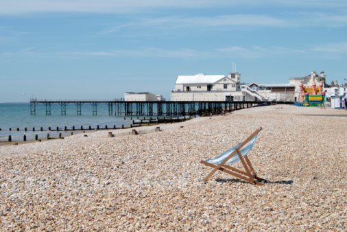 Brighton, UK - 28 March, 2021: color image depicting the exterior Victorian architecture of Brighton Palace Pier in the southeast England city of Brighton. People are sitting and socialising on the beach.