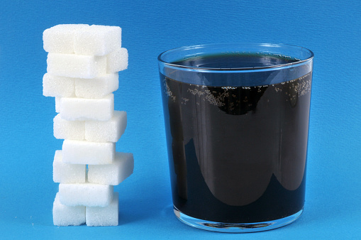 Stack of sugar stones next to a glass of soda on a blue background