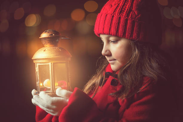 Beautiful little girl in a red winter coat walking through the snowy night with lantern