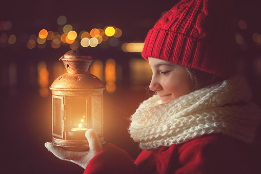 Beautiful little girl in a red winter coat walking through the snowy night with lantern