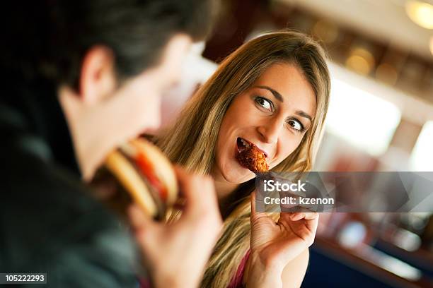 Girl Eating A Chicken Wing Smiling At A Man Eating A Burger Stock Photo - Download Image Now