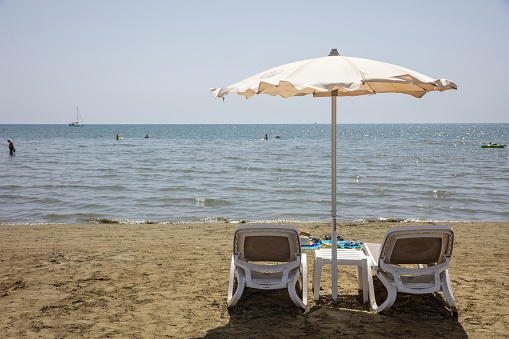 Empty deck chairs and umbrella on a sandy beach, sea water background