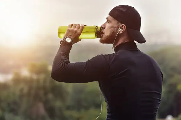Photo of Muscular bearded athlete drink a water after good workout session on city park.