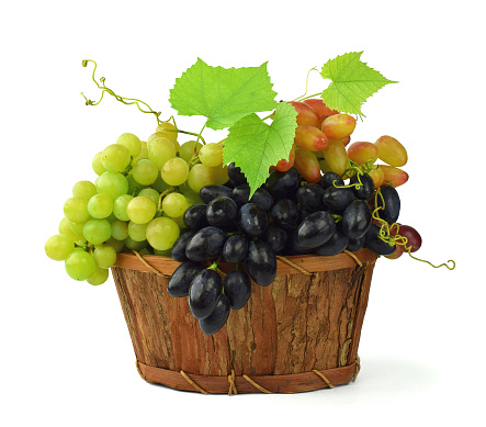 A variety of ripe grapes in a wooden basket. Isolated on white.