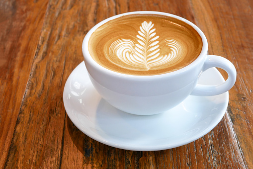 Caliente latte capuchino café con hermosa 'rosetta' latte arte espuma de la leche en el fondo de la tabla de madera rústica. photo