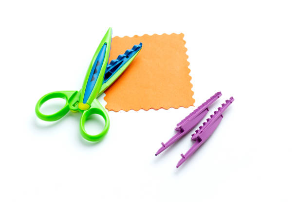 A sheet of orange paper with a wavy edge lies on a white background near the curly scissors. Creativity, playing with children at home and in kindergarten A sheet of orange paper with a wavy edge lies on a white background near the curly scissors. Creativity, playing with children at home and in kindergarten. hi res stock pictures, royalty-free photos & images