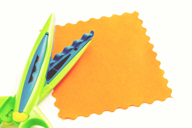 A sheet of orange paper with a wavy edge lies on a white background near the curly scissors. Creativity, playing with children at home and in kindergarten A sheet of orange paper with a wavy edge lies on a white background near the curly scissors. Creativity, playing with children at home and in kindergarten. hi res stock pictures, royalty-free photos & images