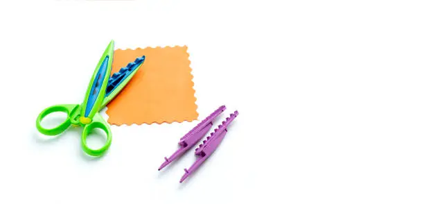 Photo of A sheet of orange paper with a wavy edge lies on a white background near the curly scissors. Creativity, playing with children at home and in kindergarten