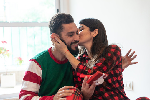 Loving man giving his partner her christmas present while she kisses him both looking very happy  and smiling