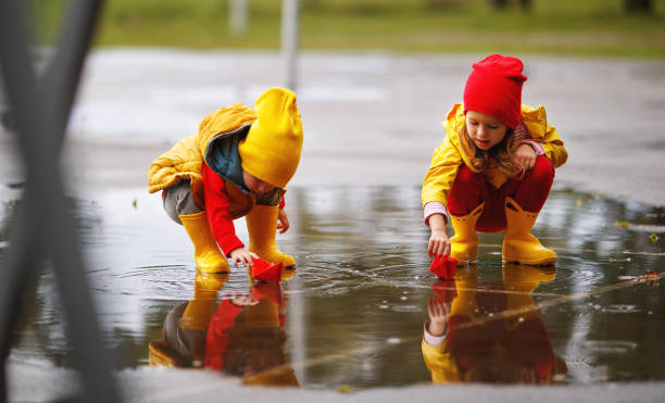 glückliche kinder mädchen und jungen mit papierboot in pfütze im herbst auf die natur - puddle rain boot water stock-fotos und bilder