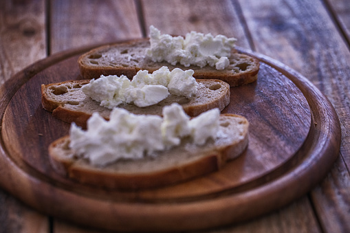 Simple breakfast, slices of rye bread with cow cheese cream spread at wood plate. Close up, selective focus