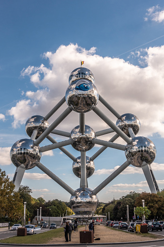 Brussels, Belgium - September 25, 2018: The voluminous Atomium monument with its shining spheres and tubes against blue sky with white cloudscape. Cars and people on the ground.