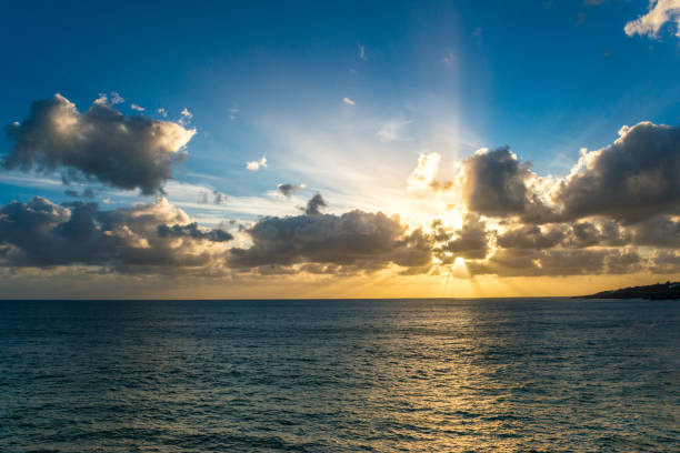 Colorful seascape image with shiny sea and sailboat over cloudy sky and sun during sunset in Cozumel, Mexico