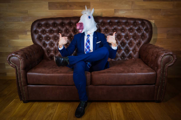 istock Funny unicorn in elegant suit sits on sofa 1052664224
