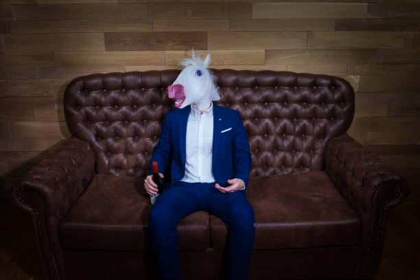 istock Funny unicorn in elegant suit sits on sofa 1052664236