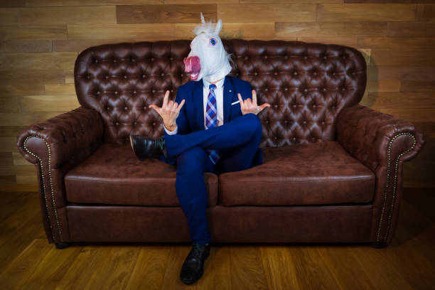 istock Funny unicorn in elegant suit sits on sofa 1052664238