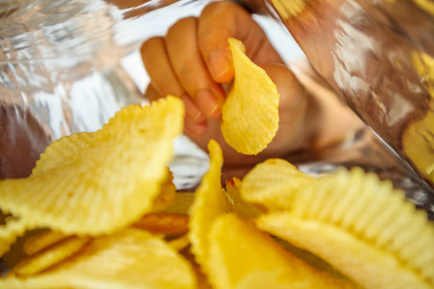 рука держать картофельные чипсы внутри закуски фольги мешок - potato chip стоковые фото и изображения