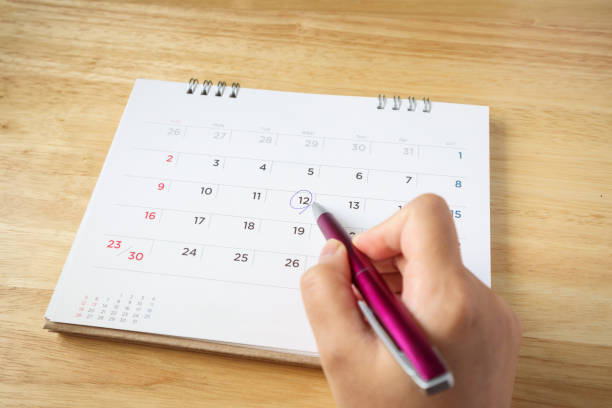 istock calendar page on table with female hand holding pen, top view 1052675644