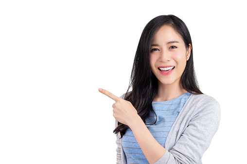 Beautiful happy confident Asian woman in casual clothes smiling and pointing hand to empty space aside, studio shot isolated on white background