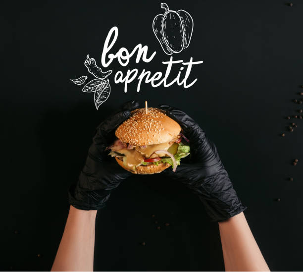 colpo di mano ritagliato in guanti con delizioso hamburger con tacchino, verdure e condimento caesar su nero con scritta "bon appetit" - bon appetite foto e immagini stock
