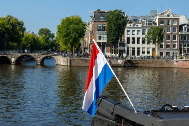 Dutch Flag Flying On Boat On Amsterdam Canal with boats and tourists