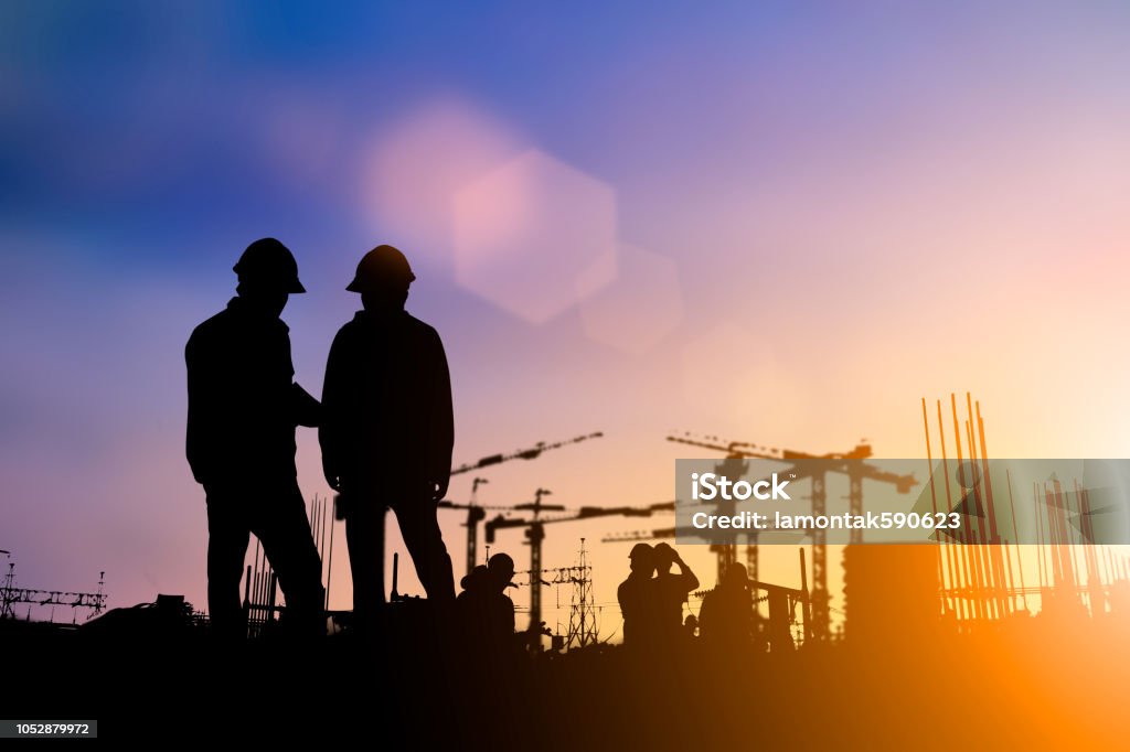 Silhouette of engineer and construction team working at site over blurred background for industry background with Light fair.Create from multiple reference images together Construction Site Stock Photo