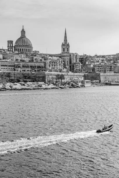 A motorboat passes along the Valletta coastline in Malta, black and white photography A motorboat passes along the Valletta coastline in Malta leaving traces on the Mediterranean Sea water surface, black and white photography st paul cathedral la valletta malta island stock pictures, royalty-free photos & images
