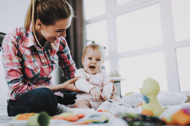 Mother Sits with Child on Floor and Holding Doll Mother Sits with Child on Floor and Holding Doll. Young Smiling Mother Wears Casual Clothes Playing Toys with Cute Caucasian Baby on Floor near Large Panoramic Window in Living Room. nanny photos stock pictures, royalty-free photos & images
