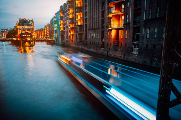 A colorfully illuminated boat cruising on the Wandrahmsfleet at night. The Warehouse District in Hamburg, Germany. The district located within the HafenCity quarter. Long exposure