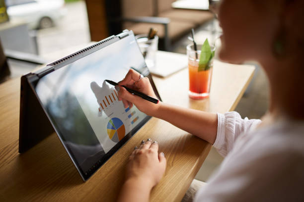 Businesswoman hand pointing with stylus on the chart over convertible laptop screen in tent mode. Woman using 2 in 1 notebook with touchscreen for work on business presentation. Isolated close view. stock photo