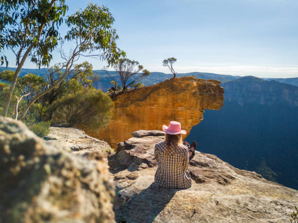 istock Female sits on cliff ledge with spectacular mountain valley views 1052983202