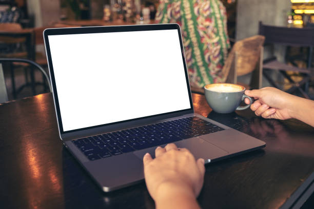 istock Mockup image of a woman's hands using laptop with blank white desktop screen while drinking hot coffee on wooden table in cafe 1052991542