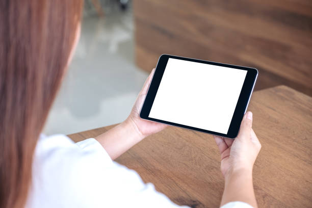 istock Mockup image of woman holding and using black tablet pc with blank white desktop screen while sitting in office 1052995298