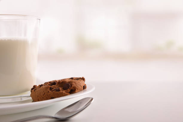 Breakfast with round biscuits with black chocolate nuggets on white table in kitchen. Front view. Horizontal composition