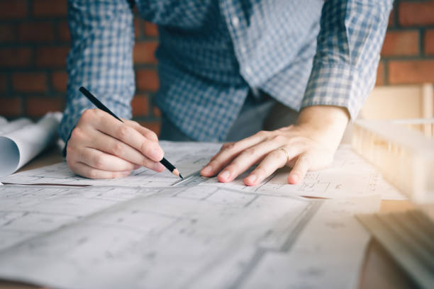 istock Interior designer or architect reviewing blueprints and holding pencil drawing on desk at home office. 1053011252